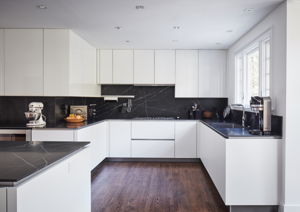 This is an example of a large modern kitchen/diner in New York with a submerged sink, glass-front cabinets, white cabinets, black splashback, stainless steel appliances, dark hardwood flooring, an island, brown floors and black worktops.