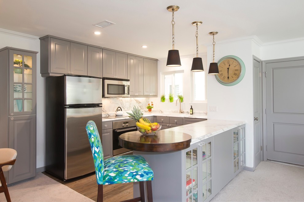 Small traditional u-shaped kitchen/diner in Orange County with a built-in sink, laminate countertops, a breakfast bar, raised-panel cabinets, grey cabinets, white splashback, stone slab splashback, stainless steel appliances, dark hardwood flooring and brown floors.