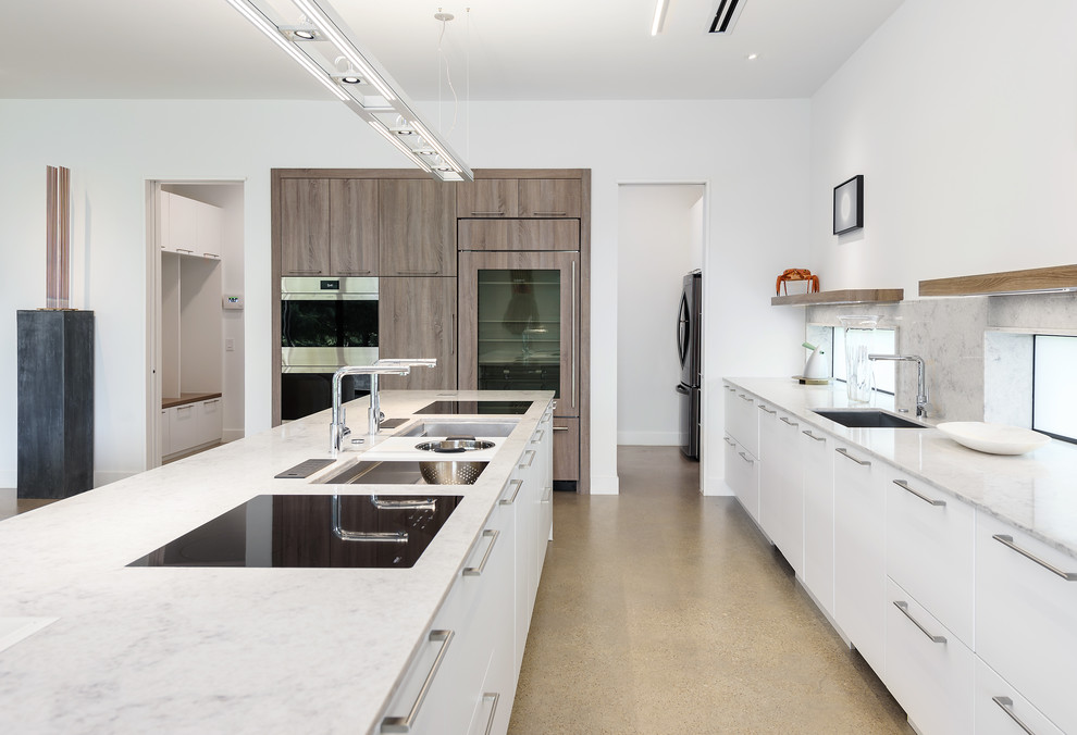Modern inredning av ett grå grått kök, med släta luckor, grått stänkskydd, en köksö, grått golv, en undermonterad diskho, vita skåp, betonggolv, fönster som stänkskydd och rostfria vitvaror