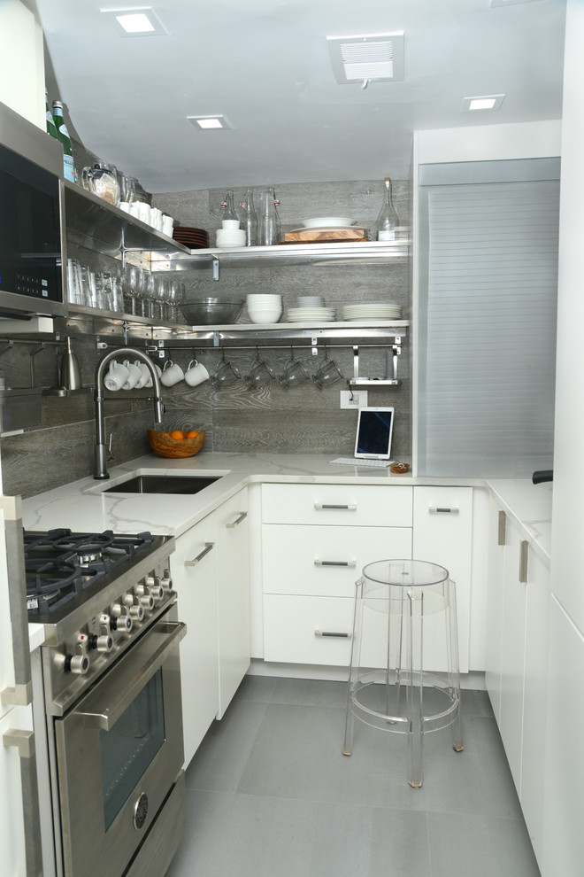 Foto på ett avskilt, litet industriellt u-kök, med en undermonterad diskho, släta luckor, vita skåp, granitbänkskiva, grått stänkskydd, stänkskydd i porslinskakel, rostfria vitvaror, klinkergolv i porslin och grått golv