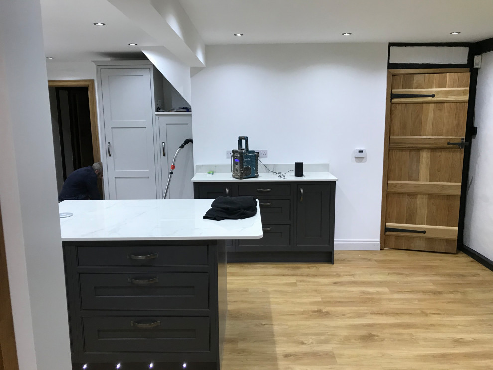 This is an example of a large traditional kitchen/diner in Hertfordshire with a submerged sink, shaker cabinets, grey cabinets, quartz worktops, white splashback, glass sheet splashback, black appliances, vinyl flooring, an island, brown floors and white worktops.