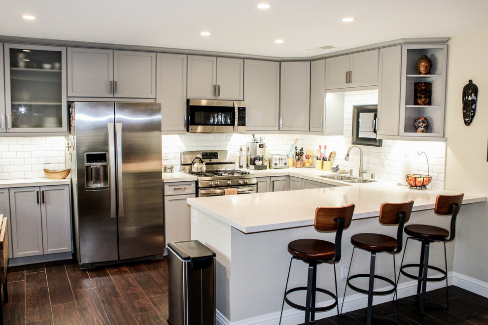 Idéer för ett litet modernt vit kök, med en undermonterad diskho, luckor med infälld panel, grå skåp, bänkskiva i kvarts, vitt stänkskydd, stänkskydd i tunnelbanekakel, rostfria vitvaror, klinkergolv i porslin, en halv köksö och brunt golv