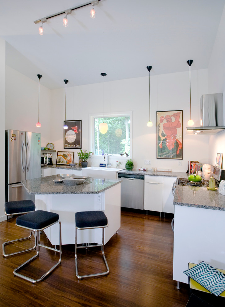 Moderne Wohnküche in U-Form mit Landhausspüle, flächenbündigen Schrankfronten, weißen Schränken, Küchengeräten aus Edelstahl, dunklem Holzboden und Kücheninsel in New York
