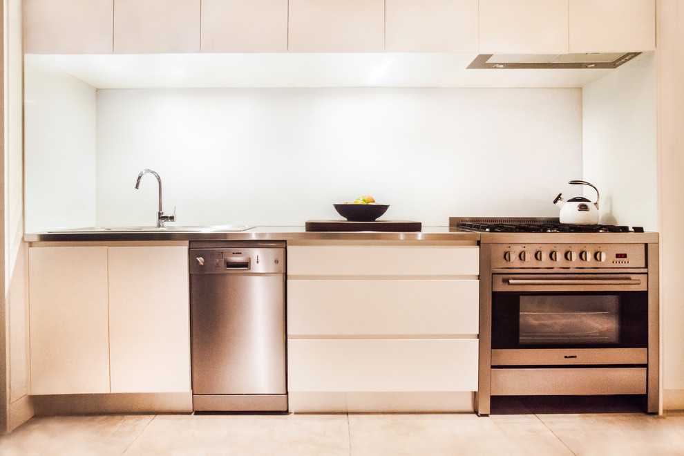 Idéer för att renovera ett litet funkis kök, med en dubbel diskho, luckor med infälld panel, vita skåp, bänkskiva i rostfritt stål, vitt stänkskydd, glaspanel som stänkskydd, rostfria vitvaror och betonggolv