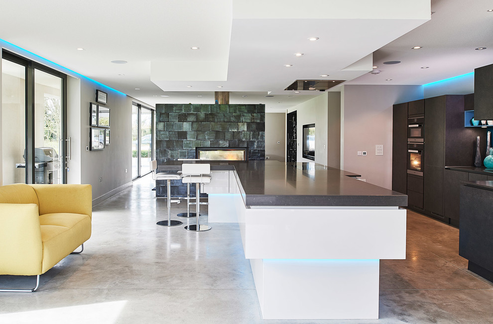 Large contemporary single-wall open plan kitchen in Other with flat-panel cabinets, concrete flooring, an island, grey floors, grey worktops, a built-in sink, grey cabinets, blue splashback, glass sheet splashback and stainless steel appliances.