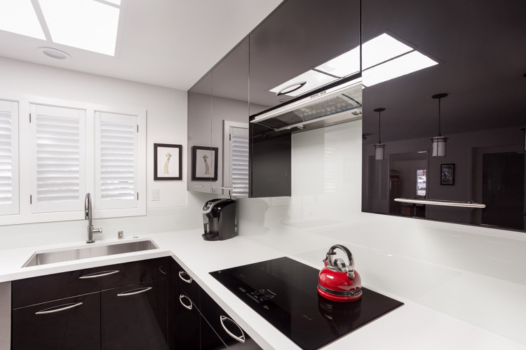 Bild på ett funkis u-kök, med en undermonterad diskho, släta luckor, svarta skåp, vitt stänkskydd, glaspanel som stänkskydd, rostfria vitvaror och en halv köksö