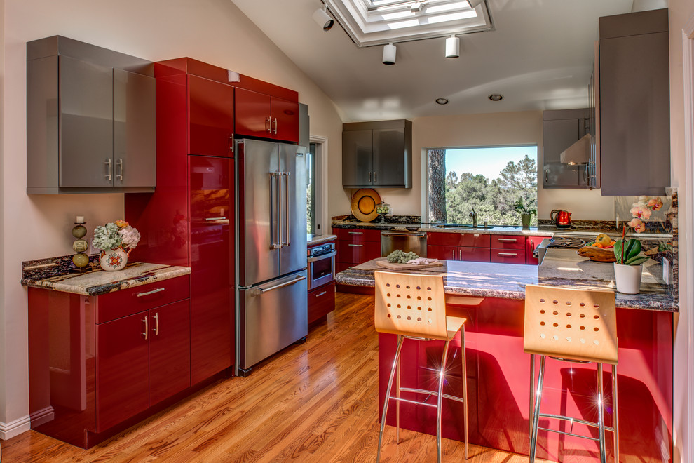 Exemple d'une cuisine moderne de taille moyenne avec un évier encastré, un placard à porte plane, des portes de placard rouges, un plan de travail en granite, un électroménager en acier inoxydable, un sol en bois brun et une péninsule.