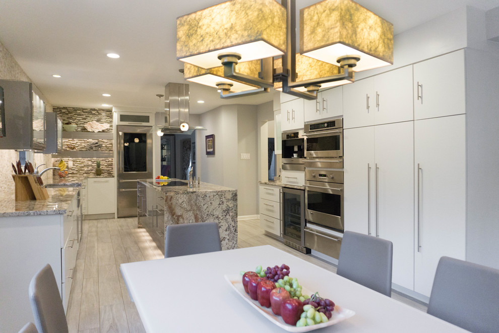 Eat-in kitchen - large contemporary galley ceramic tile and beige floor eat-in kitchen idea in Philadelphia with a farmhouse sink, glass-front cabinets, white cabinets, granite countertops, multicolored backsplash, glass tile backsplash, stainless steel appliances and an island