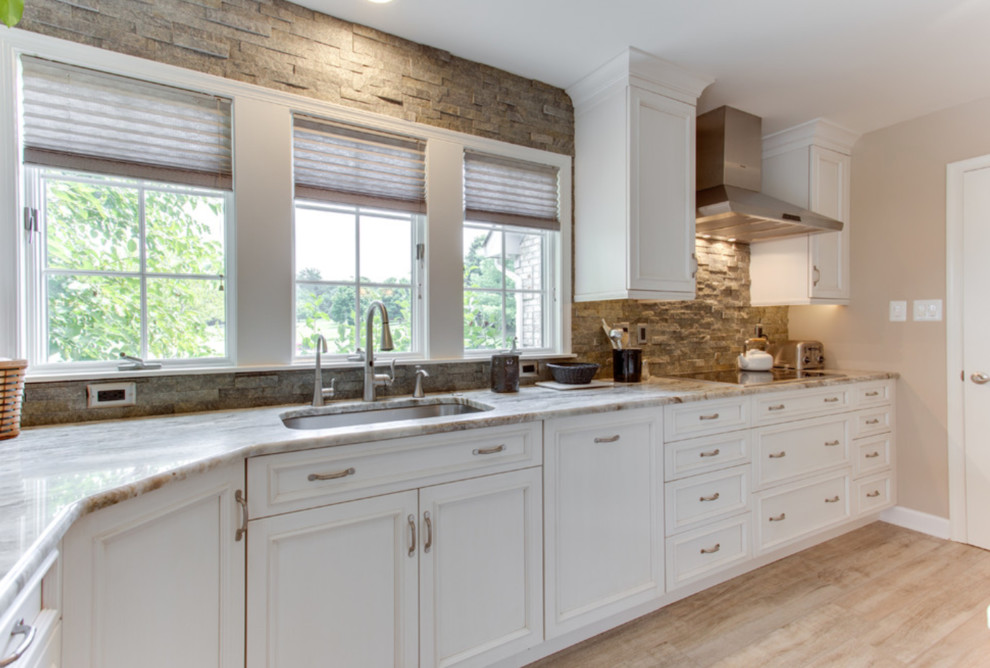 Inredning av ett klassiskt stort grå grått kök, med en undermonterad diskho, luckor med infälld panel, vita skåp, granitbänkskiva, brunt stänkskydd, stänkskydd i stenkakel, rostfria vitvaror, ljust trägolv och beiget golv