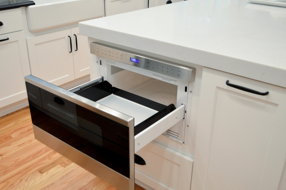 Réalisation d'une cuisine encastrable tradition en U fermée et de taille moyenne avec un évier de ferme, un placard à porte shaker, des portes de placard blanches, un plan de travail en granite, une crédence blanche, une crédence en carreau de porcelaine, un sol en bois brun, îlot, un sol marron et plan de travail noir.