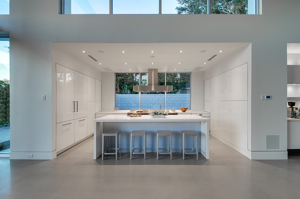 Cette photo montre une cuisine encastrable moderne avec un placard à porte plane, des portes de placard blanches, sol en béton ciré et îlot.