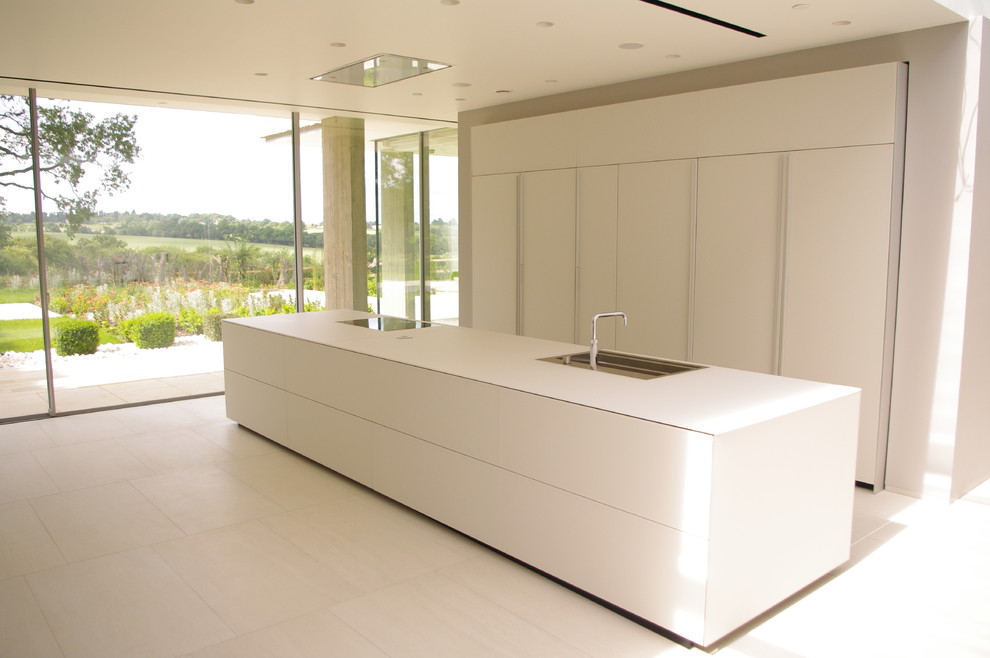 Exemple d'une cuisine américaine parallèle tendance avec un évier encastré, un placard à porte plane, des portes de placard blanches, un plan de travail en verre, un sol en carrelage de porcelaine et îlot.
