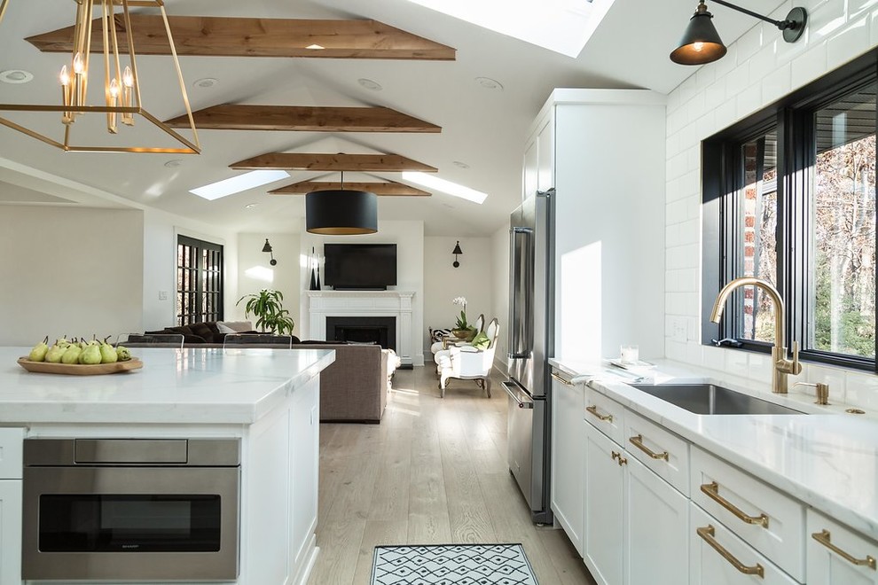 Example of a large transitional l-shaped light wood floor and brown floor kitchen design in Chicago with an undermount sink, shaker cabinets, white cabinets, quartz countertops, gray backsplash, marble backsplash, stainless steel appliances and an island
