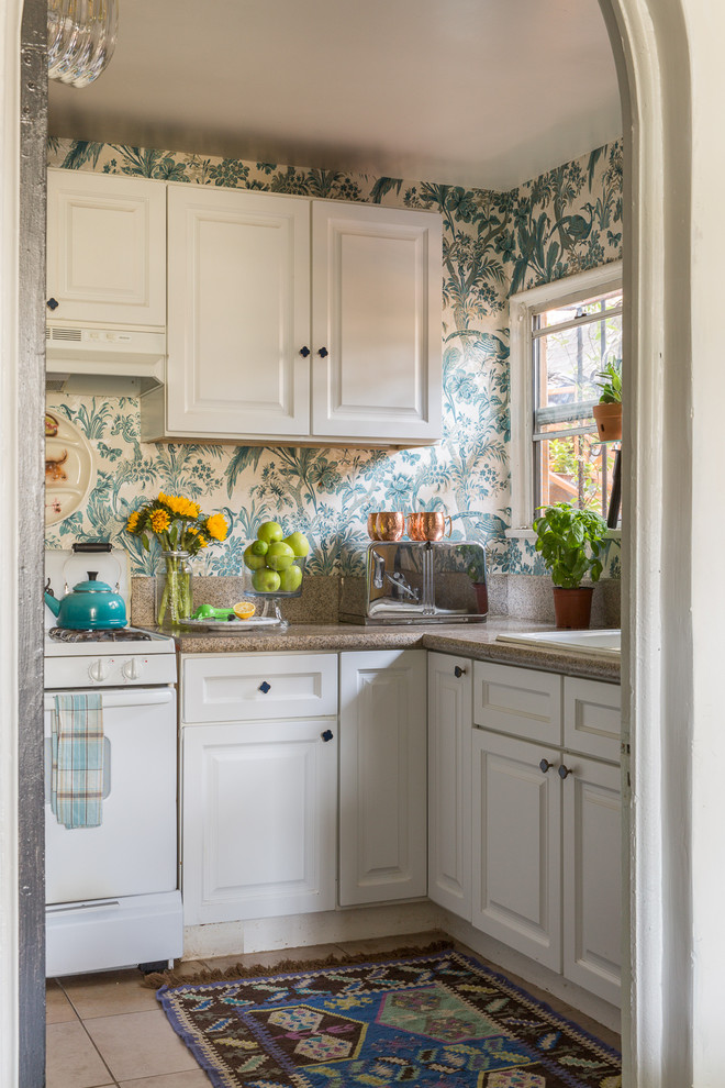 Enclosed kitchen - small traditional l-shaped beige floor enclosed kitchen idea in Los Angeles with a drop-in sink, raised-panel cabinets, white cabinets, multicolored backsplash, white appliances, no island and brown countertops