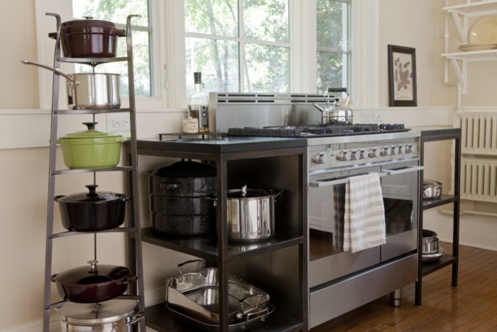 Cette image montre une petite cuisine américaine rustique en L avec un évier de ferme, un placard à porte shaker, des portes de placard blanches, un électroménager en acier inoxydable, un sol en bois brun et îlot.