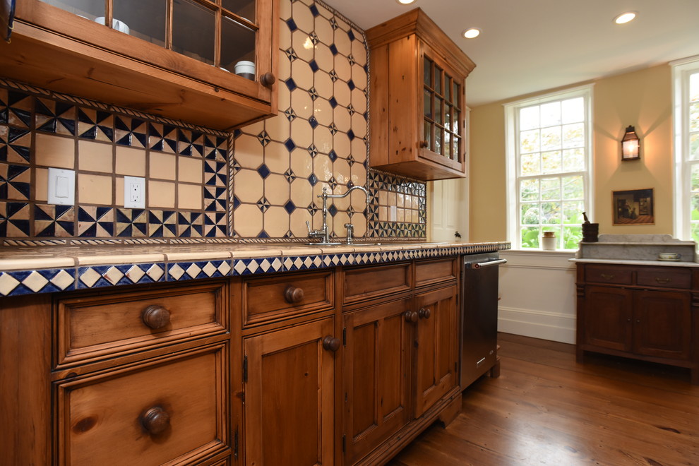 Bild på ett avskilt, stort amerikanskt l-kök, med en nedsänkt diskho, luckor med infälld panel, skåp i mellenmörkt trä, kaklad bänkskiva, flerfärgad stänkskydd, stänkskydd i mosaik, rostfria vitvaror, mellanmörkt trägolv och brunt golv