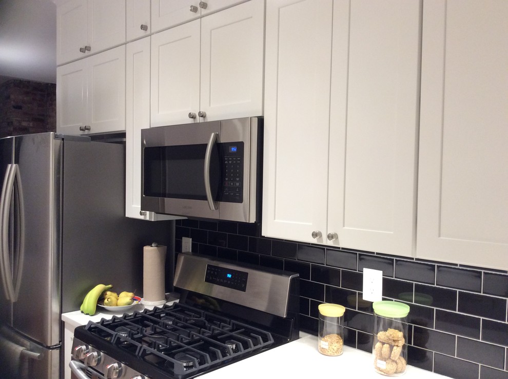 Example of a small minimalist galley plywood floor and beige floor kitchen pantry design in New York with an undermount sink, recessed-panel cabinets, white cabinets, black backsplash, subway tile backsplash, stainless steel appliances, an island and quartzite countertops