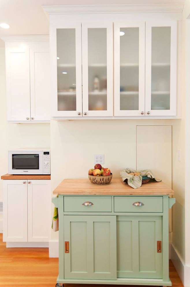 This is an example of a medium sized midcentury u-shaped kitchen/diner in Boston with a belfast sink, shaker cabinets, white cabinets, wood worktops, blue splashback, glass tiled splashback, white appliances, medium hardwood flooring and a breakfast bar.