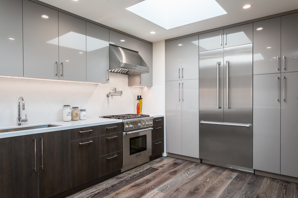 Bild på ett mellanstort funkis kök, med en undermonterad diskho, släta luckor, grå skåp, bänkskiva i kvarts, vitt stänkskydd, stänkskydd i sten, rostfria vitvaror, mörkt trägolv och en köksö