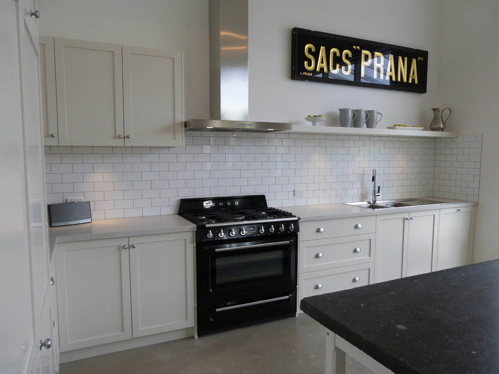 Mid-sized elegant l-shaped concrete floor and gray floor eat-in kitchen photo in Adelaide with a double-bowl sink, shaker cabinets, white cabinets, quartz countertops, white backsplash, ceramic backsplash, black appliances and an island
