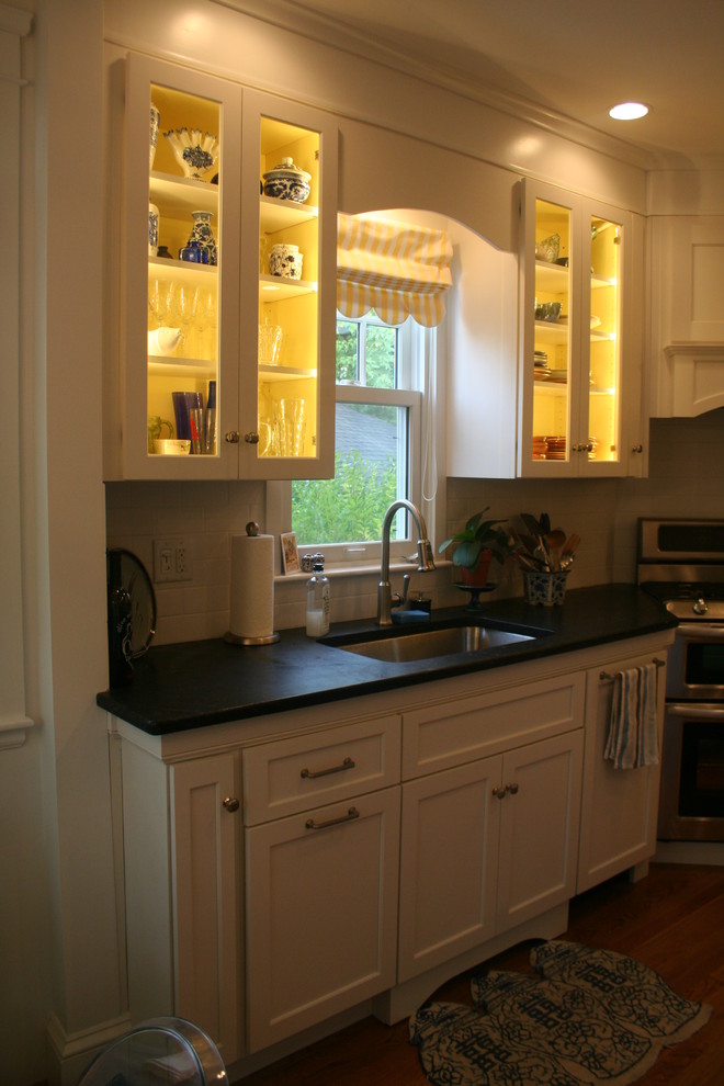 Example of a small eclectic l-shaped light wood floor eat-in kitchen design in Providence with an undermount sink, shaker cabinets, white cabinets, soapstone countertops, white backsplash, ceramic backsplash, paneled appliances and an island