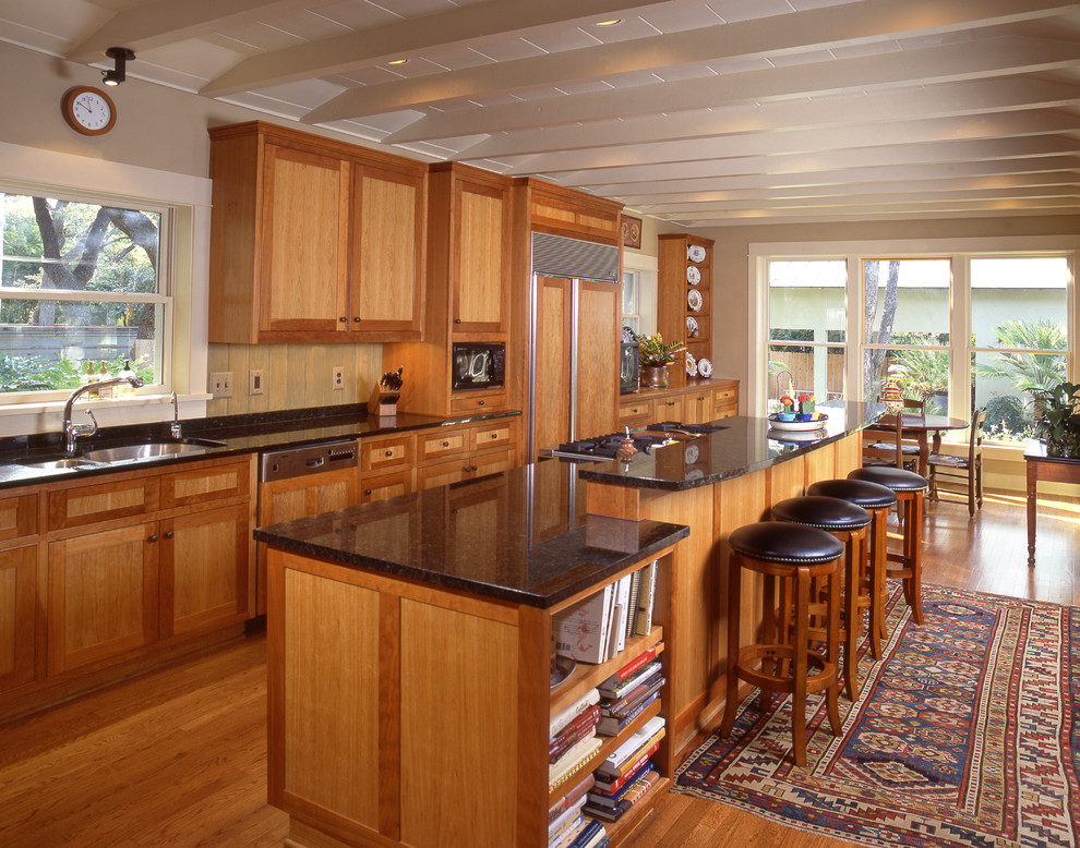 Foto på ett mellanstort amerikanskt kök, med en undermonterad diskho, skåp i shakerstil, skåp i ljust trä, granitbänkskiva, svart stänkskydd, rostfria vitvaror, ljust trägolv och en köksö