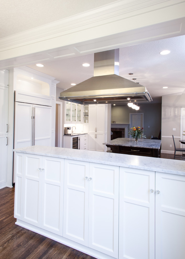 Inredning av ett klassiskt stort kök, med en undermonterad diskho, luckor med infälld panel, vita skåp, marmorbänkskiva, grått stänkskydd, rostfria vitvaror, mellanmörkt trägolv, en köksö och stänkskydd i stenkakel