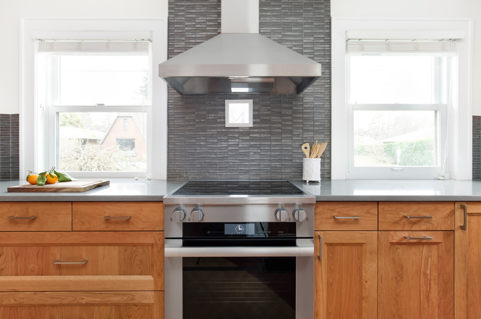 Inredning av ett eklektiskt avskilt, litet grå grått u-kök, med en undermonterad diskho, skåp i shakerstil, skåp i mellenmörkt trä, bänkskiva i kvarts, grått stänkskydd, stänkskydd i glaskakel, rostfria vitvaror, en köksö och flerfärgat golv