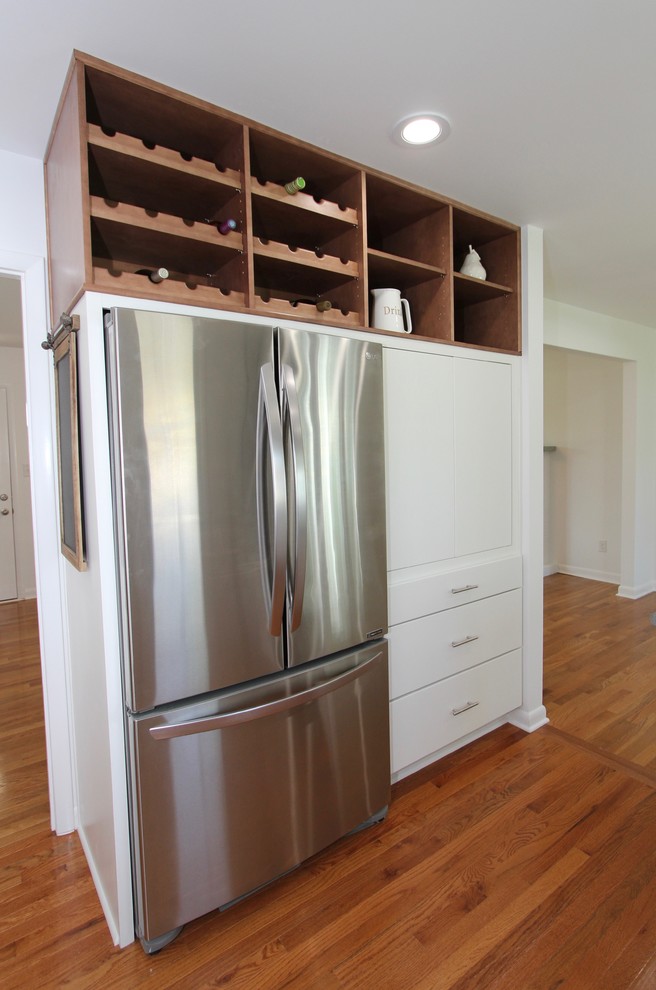 Foto på ett mellanstort lantligt grå kök, med en undermonterad diskho, släta luckor, vita skåp, bänkskiva i kvarts, vitt stänkskydd, stänkskydd i mosaik, rostfria vitvaror, mellanmörkt trägolv, en halv köksö och brunt golv