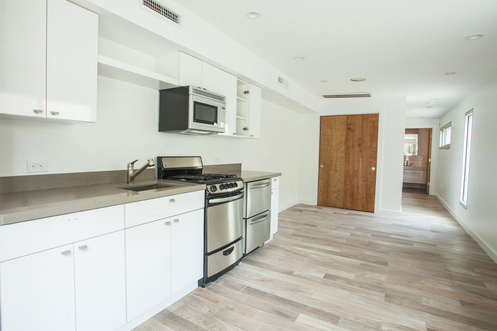 This is an example of a contemporary single-wall kitchen/diner in New York with a submerged sink, flat-panel cabinets, white cabinets, quartz worktops and stainless steel appliances.