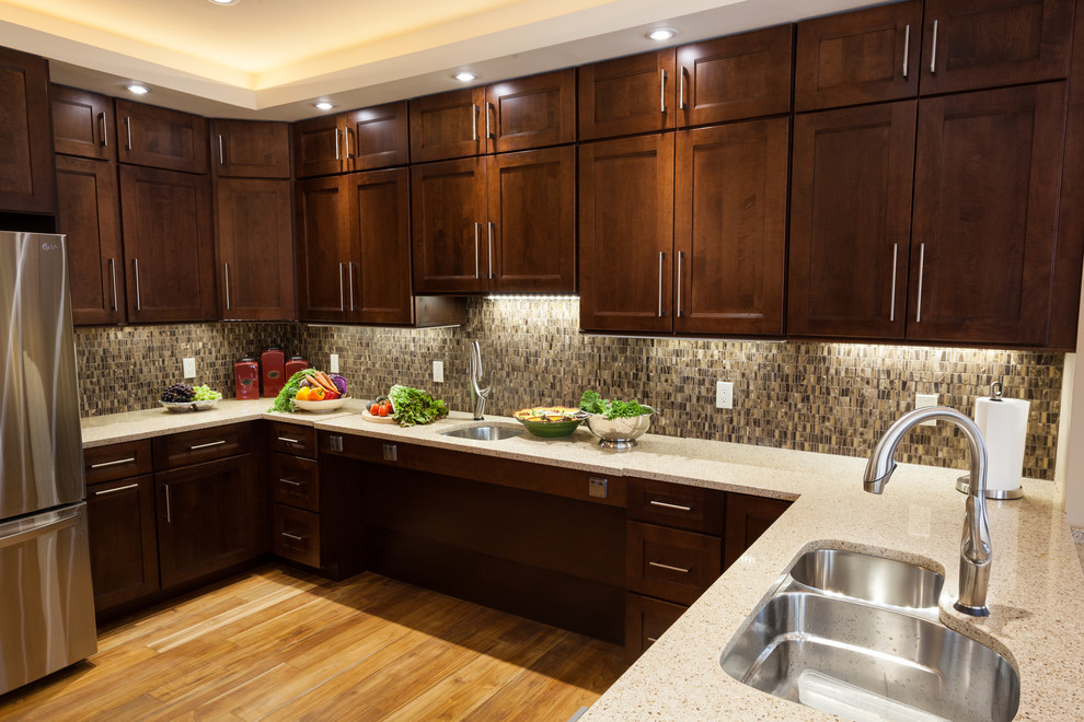 This is an example of a medium sized traditional enclosed kitchen in DC Metro with a double-bowl sink, shaker cabinets, medium wood cabinets, engineered stone countertops, brown splashback, ceramic splashback, stainless steel appliances, light hardwood flooring and an island.