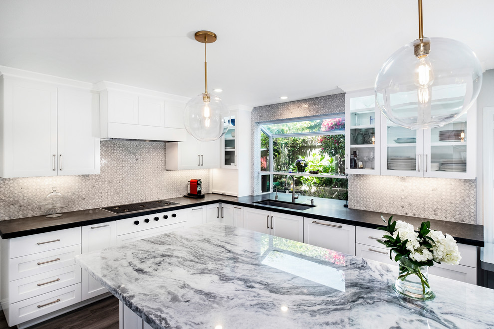 This is an example of a large classic u-shaped kitchen/diner in San Diego with a submerged sink, recessed-panel cabinets, white cabinets, granite worktops, grey splashback, glass tiled splashback, black appliances, porcelain flooring, an island, brown floors and black worktops.