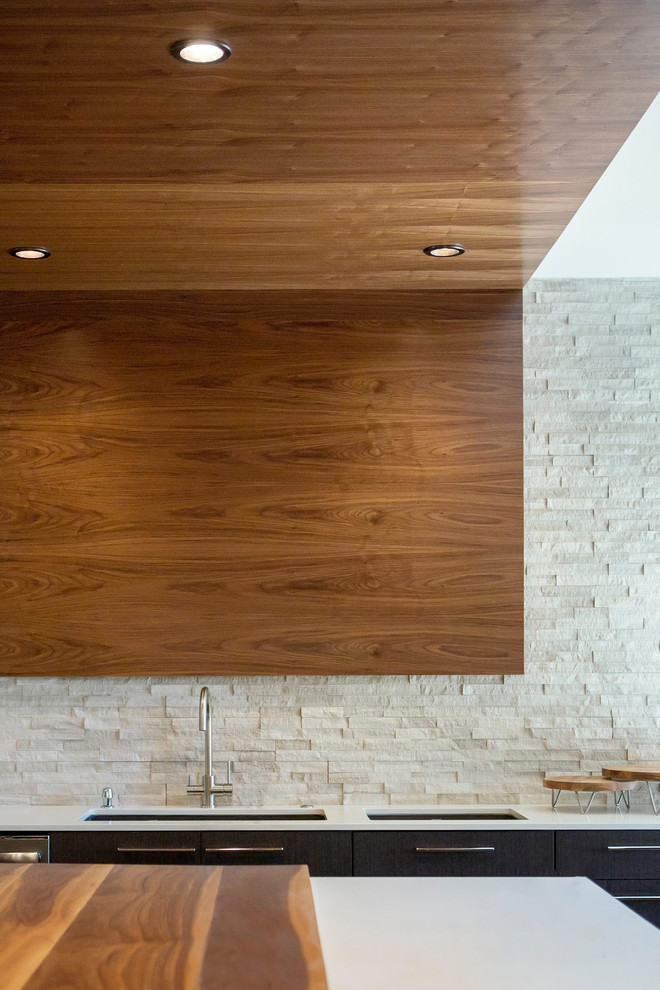 Cette image montre une grande cuisine minimaliste en U avec un placard à porte plane, un plan de travail en quartz modifié, un électroménager en acier inoxydable, un sol en bois brun, îlot et un plan de travail blanc.