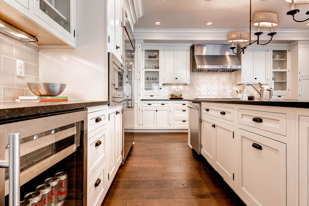 Medium sized traditional l-shaped kitchen/diner in Denver with a submerged sink, shaker cabinets, white cabinets, composite countertops, beige splashback, porcelain splashback, stainless steel appliances, medium hardwood flooring and an island.