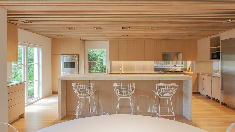 Immagine di una cucina design con ante lisce, ante in legno chiaro, elettrodomestici in acciaio inossidabile, parquet chiaro, pavimento beige e top beige