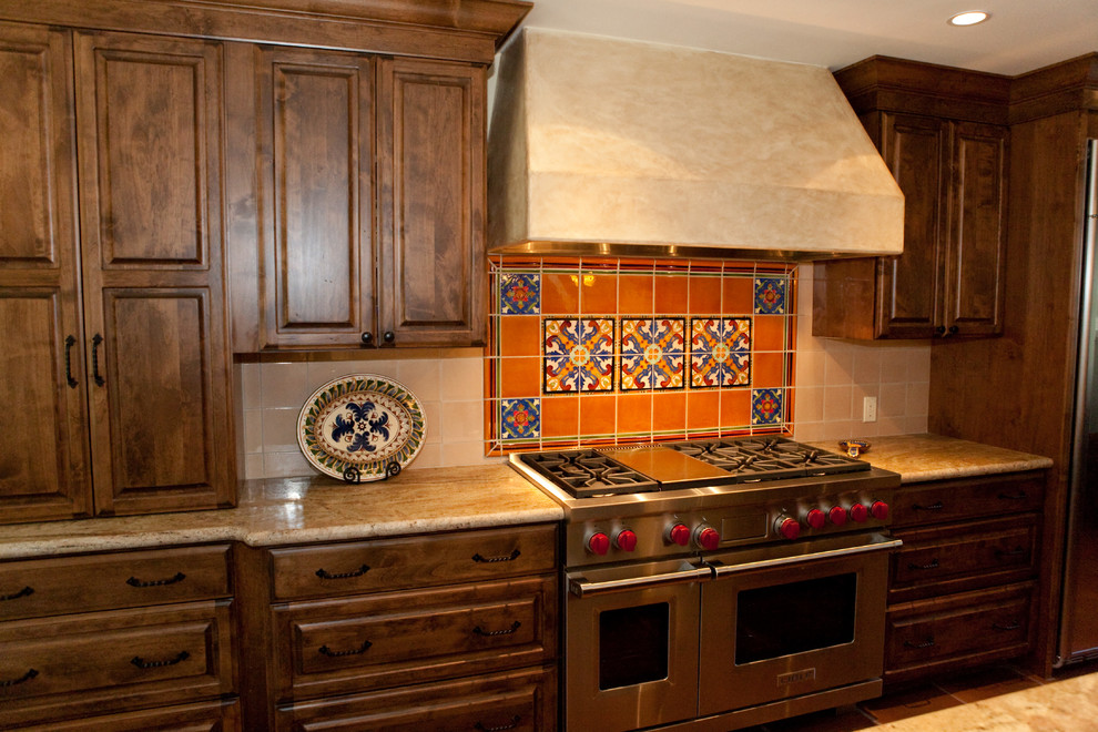 Inredning av ett medelhavsstil mellanstort brun brunt kök, med luckor med upphöjd panel, skåp i mörkt trä, granitbänkskiva, rött stänkskydd, stänkskydd i keramik, rostfria vitvaror, en köksö och brunt golv