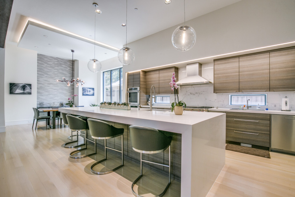Inspiration for a contemporary u-shaped kitchen/diner in Dallas with a submerged sink, flat-panel cabinets, medium wood cabinets, stainless steel appliances, light hardwood flooring, an island, beige floors and white worktops.