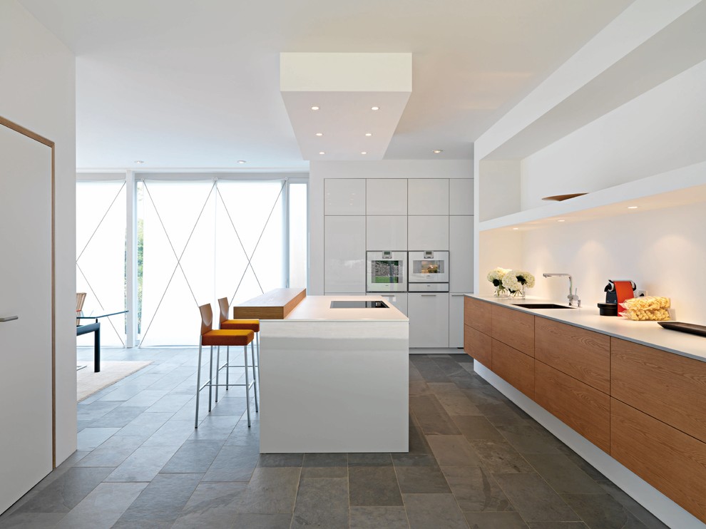 Zweizeilige Moderne Wohnküche mit flächenbündigen Schrankfronten, hellbraunen Holzschränken, weißen Elektrogeräten und Schieferboden in Los Angeles
