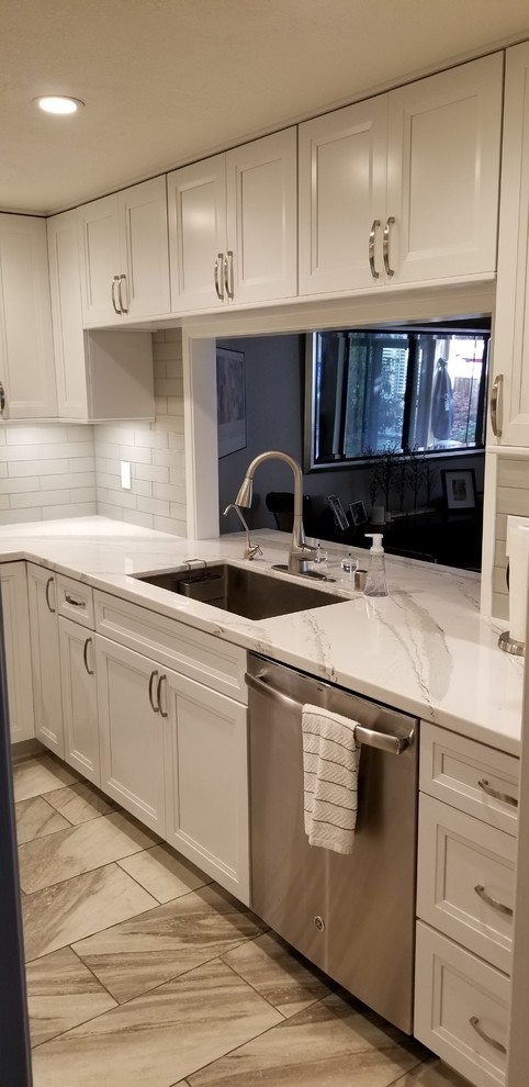 Small contemporary u-shaped enclosed kitchen in San Francisco with a submerged sink, recessed-panel cabinets, white cabinets, engineered stone countertops, white splashback, glass tiled splashback, stainless steel appliances, porcelain flooring and white floors.