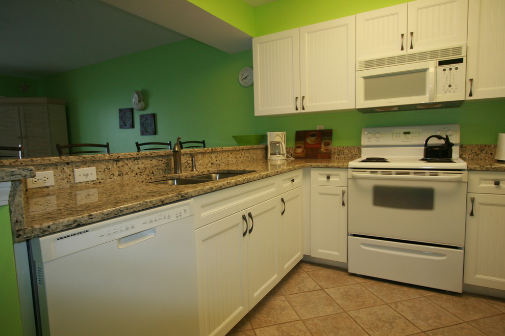 Inredning av ett maritimt litet, avskilt u-kök, med en dubbel diskho, luckor med lamellpanel, vita skåp, granitbänkskiva, grönt stänkskydd, vita vitvaror, klinkergolv i keramik och en halv köksö