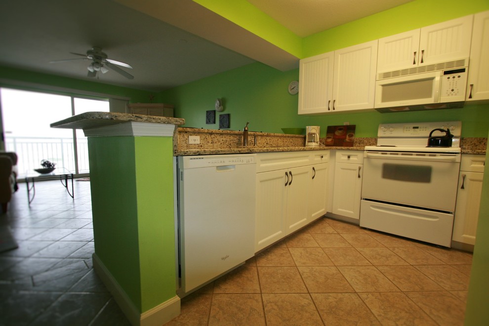 Maritim inredning av ett litet, avskilt u-kök, med en dubbel diskho, luckor med lamellpanel, vita skåp, granitbänkskiva, grönt stänkskydd, vita vitvaror, klinkergolv i keramik och en halv köksö