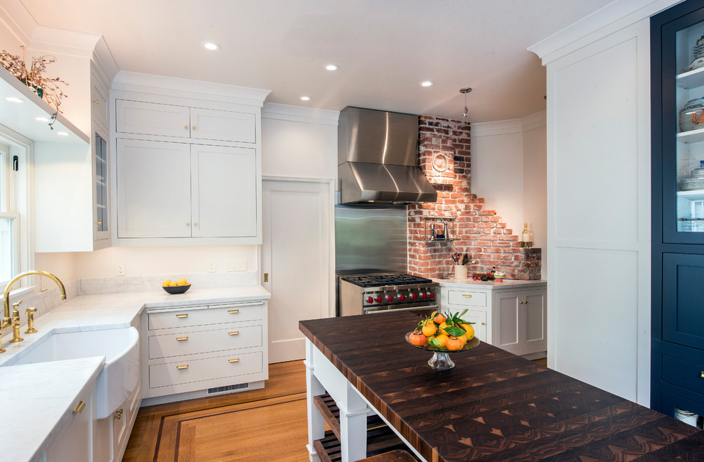 Inredning av ett amerikanskt mellanstort, avskilt vit vitt l-kök, med en rustik diskho, mellanmörkt trägolv, brunt golv, luckor med profilerade fronter, vita skåp, marmorbänkskiva, rostfria vitvaror och en köksö