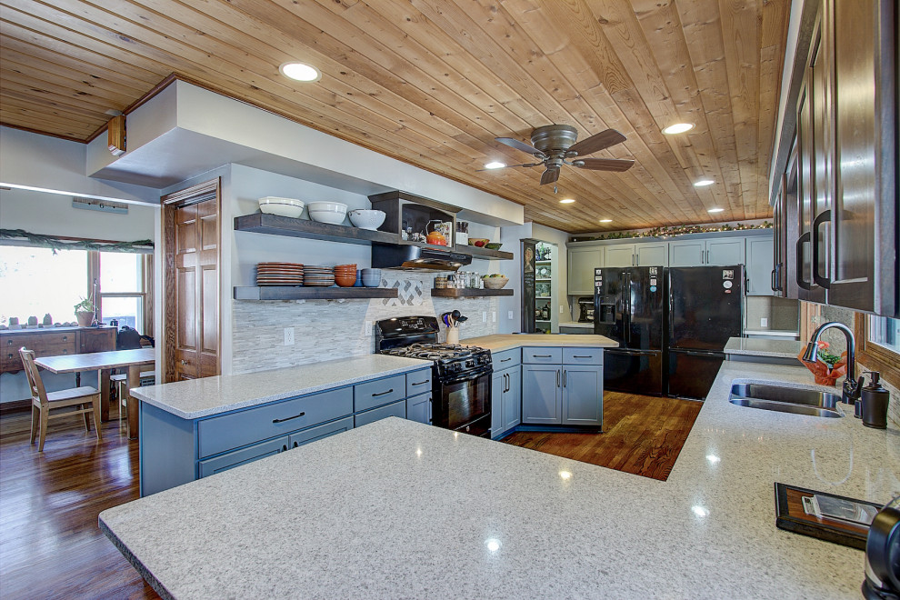 Klassisk inredning av ett mellanstort vit vitt kök, med en undermonterad diskho, skåp i shakerstil, grå skåp, bänkskiva i kvarts, grått stänkskydd, stänkskydd i stenkakel, svarta vitvaror, mellanmörkt trägolv, en halv köksö och brunt golv