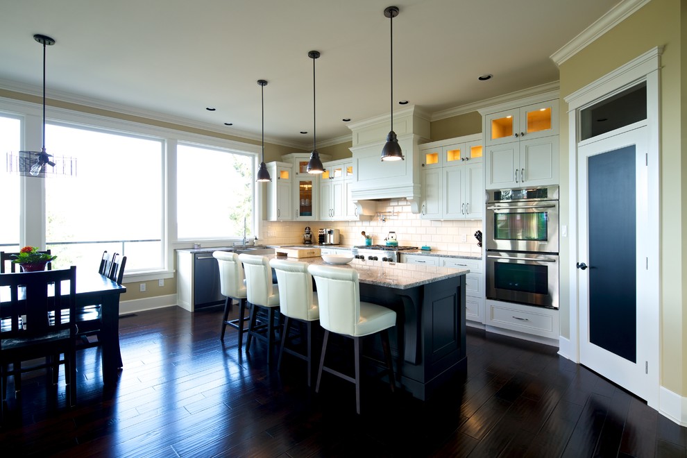 Example of a mid-sized ornate l-shaped dark wood floor open concept kitchen design in Vancouver with recessed-panel cabinets, white cabinets, quartzite countertops, beige backsplash, ceramic backsplash, stainless steel appliances, an island and an undermount sink