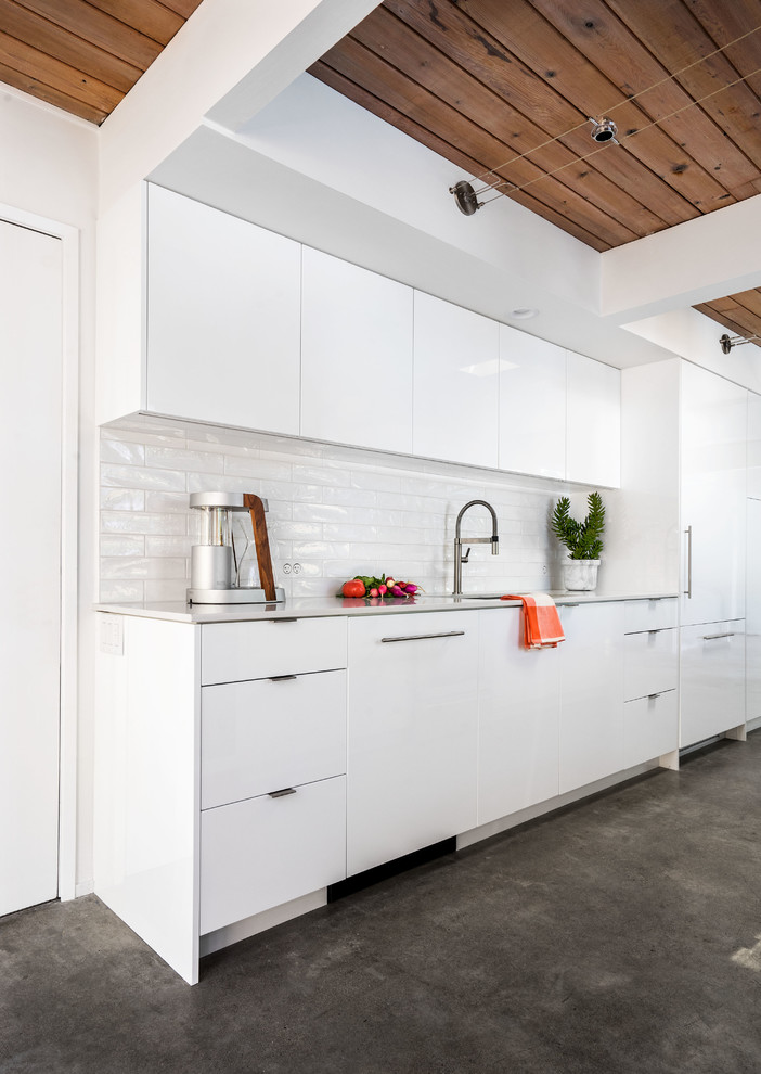 Bild på ett litet 60 tals kök, med en enkel diskho, släta luckor, vita skåp, bänkskiva i kvarts, vitt stänkskydd, stänkskydd i keramik, integrerade vitvaror, betonggolv och en köksö