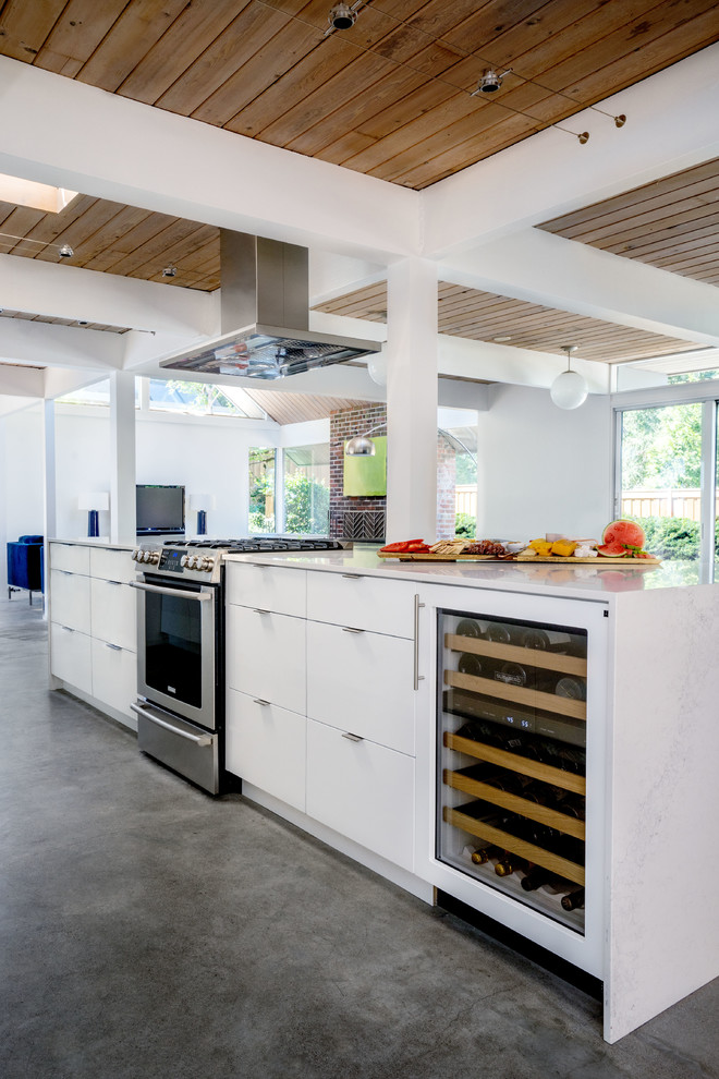 Foto på ett litet 50 tals kök, med släta luckor, vita skåp, bänkskiva i kvarts, vitt stänkskydd, stänkskydd i keramik, rostfria vitvaror, betonggolv och en köksö