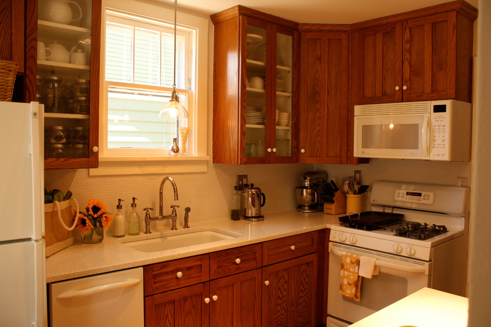 Inredning av ett lantligt kök, med en undermonterad diskho, luckor med infälld panel, skåp i mellenmörkt trä, bänkskiva i kvarts, vitt stänkskydd, stänkskydd i mosaik och vita vitvaror