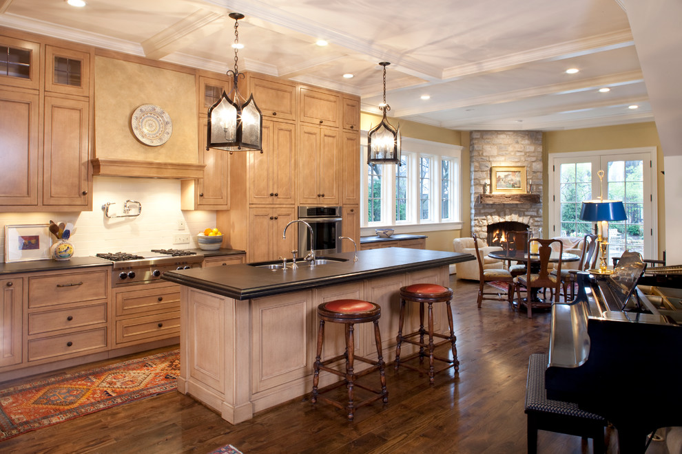 Bild på ett kök och matrum, med en dubbel diskho, luckor med infälld panel, skåp i ljust trä, vitt stänkskydd, stänkskydd i keramik, rostfria vitvaror, mörkt trägolv, en köksö och granitbänkskiva