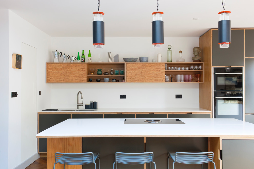 Scandinavian kitchen in London with a double-bowl sink, flat-panel cabinets, grey cabinets, white splashback, black appliances, dark hardwood flooring, an island, brown floors and white worktops.