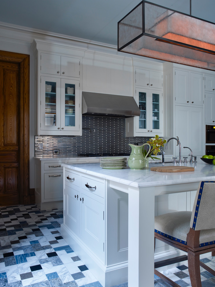 Inredning av ett klassiskt avskilt, stort grå linjärt grått kök, med luckor med infälld panel, vita skåp, marmorbänkskiva, stänkskydd med metallisk yta, stänkskydd i metallkakel, marmorgolv, en köksö och flerfärgat golv